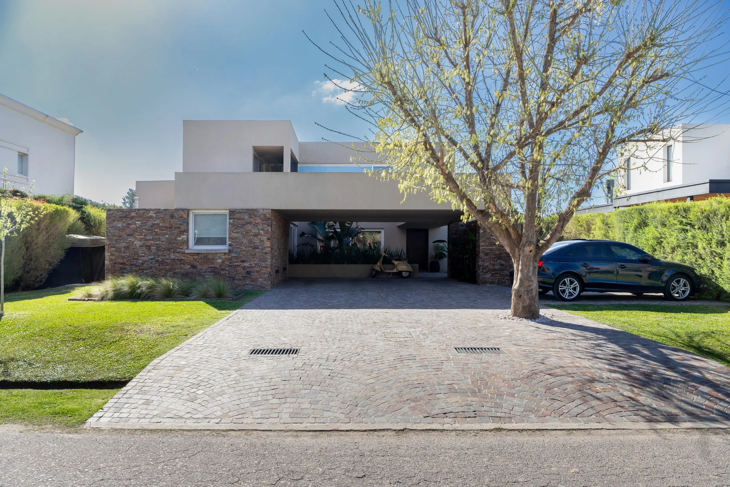 Frente de la casa con la cochera, un árbol y el acceso de adoquines