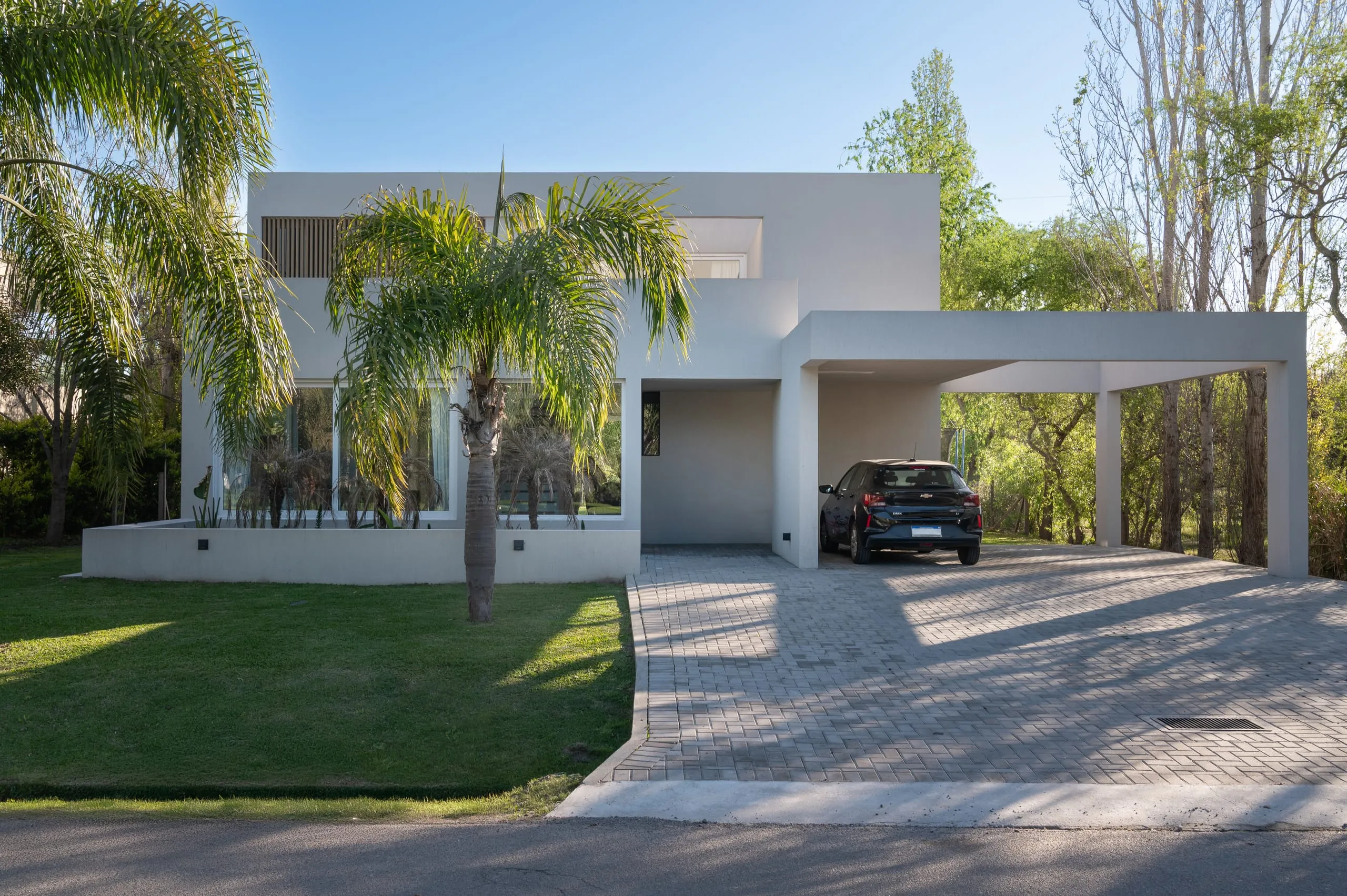 Fachada de acceso con palmera y cochera cubierta por una pérgola blanca