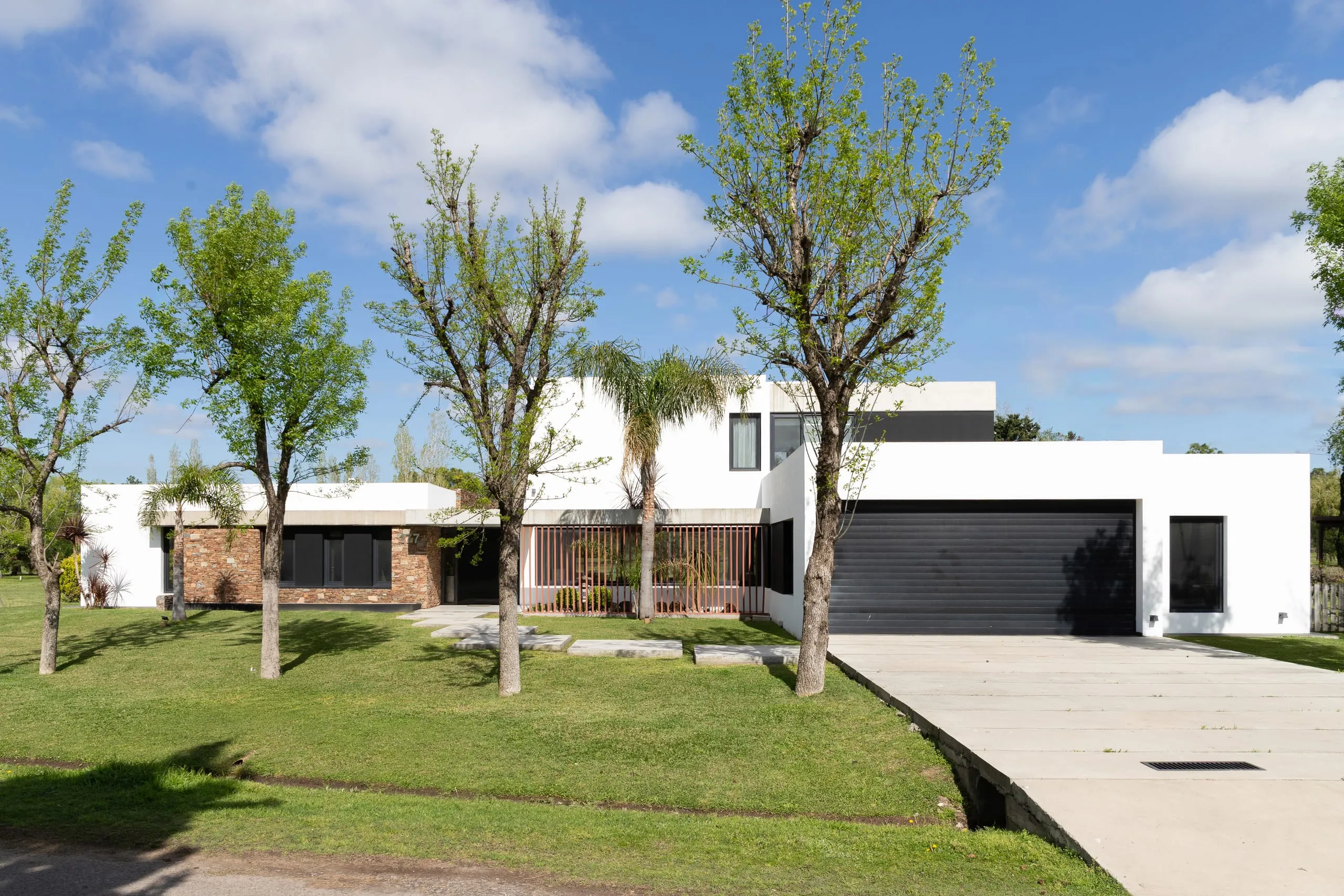 Frente de la casa con el portón negro de la cochera, jardín y árboles