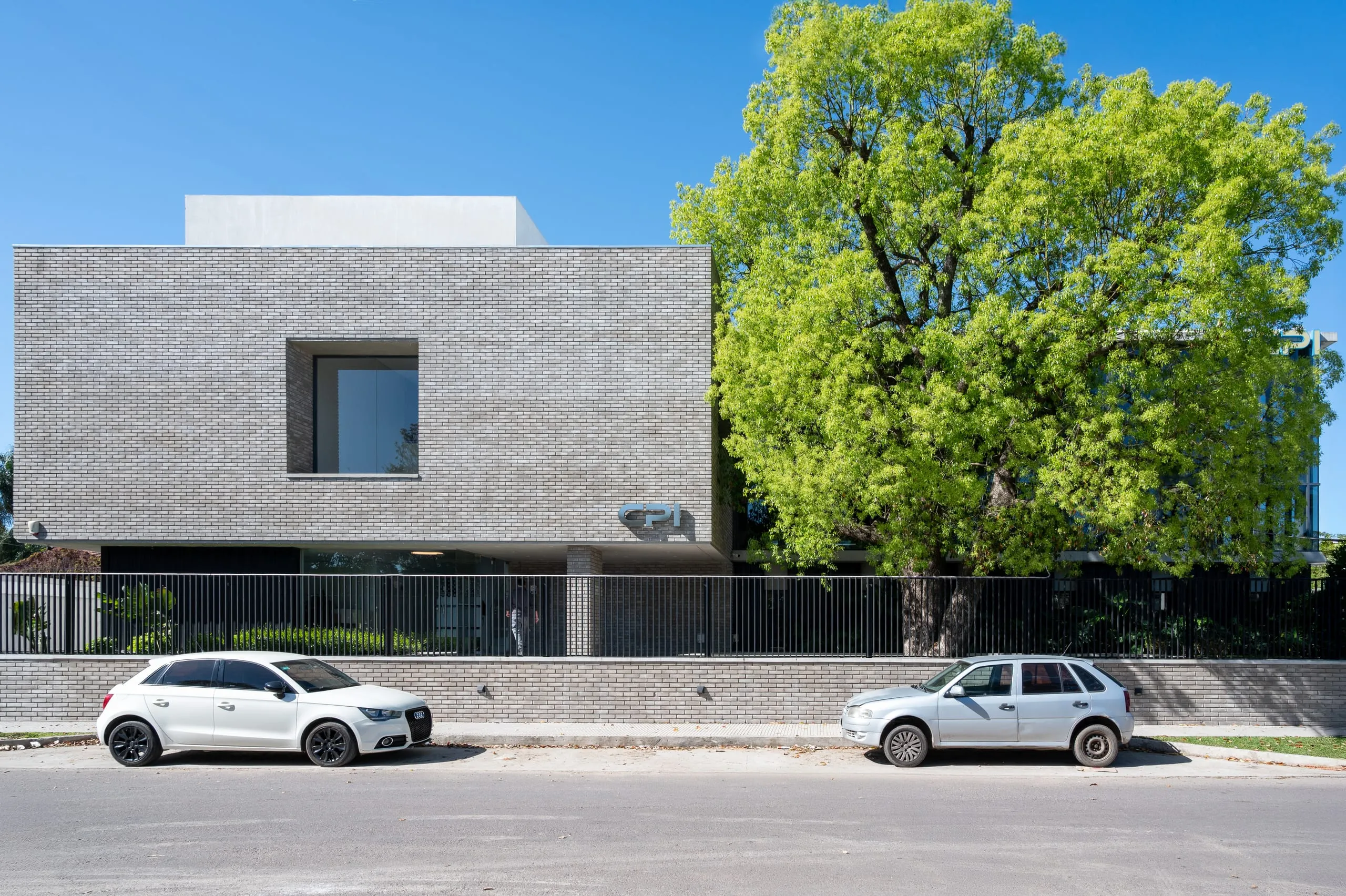 Fachada del edificio con volumen de ladrillo gris y un gran árbol