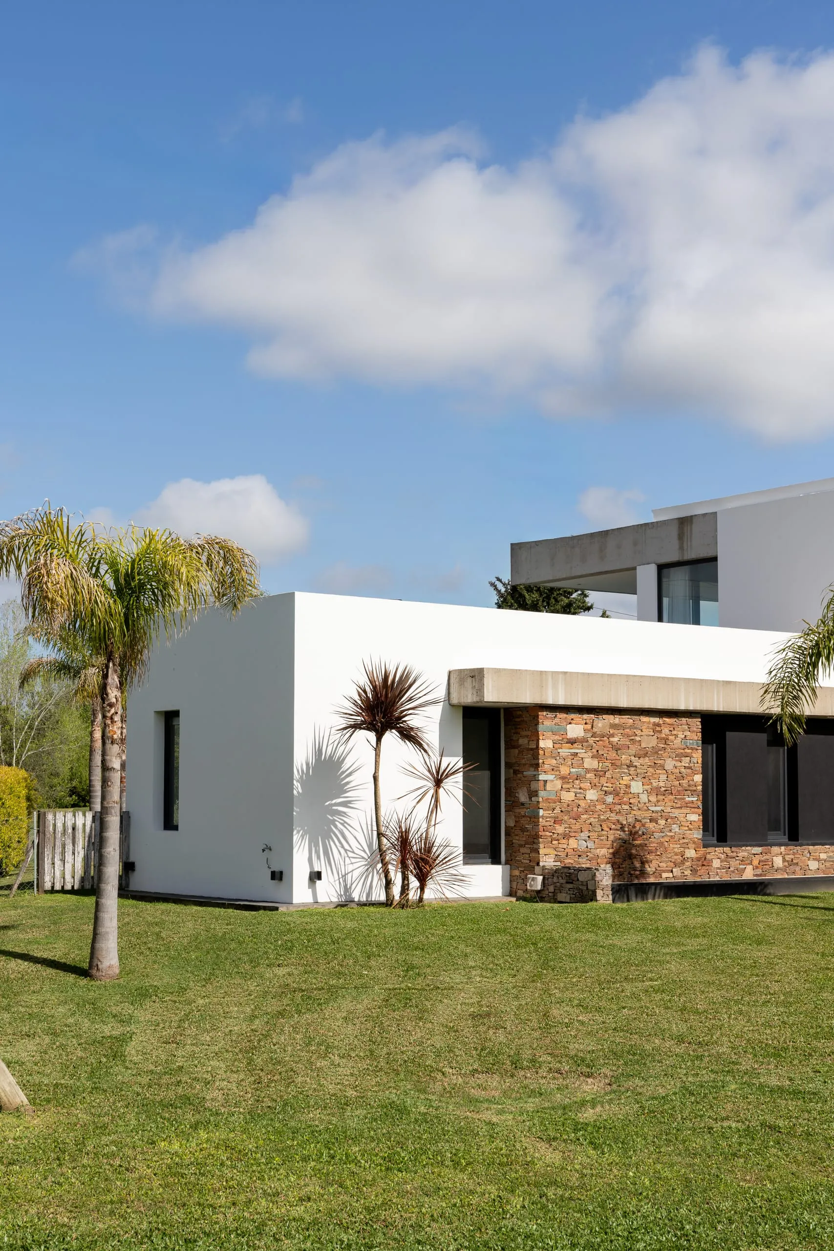 Esquina de la casa con revestimiento de piedra y palmeras