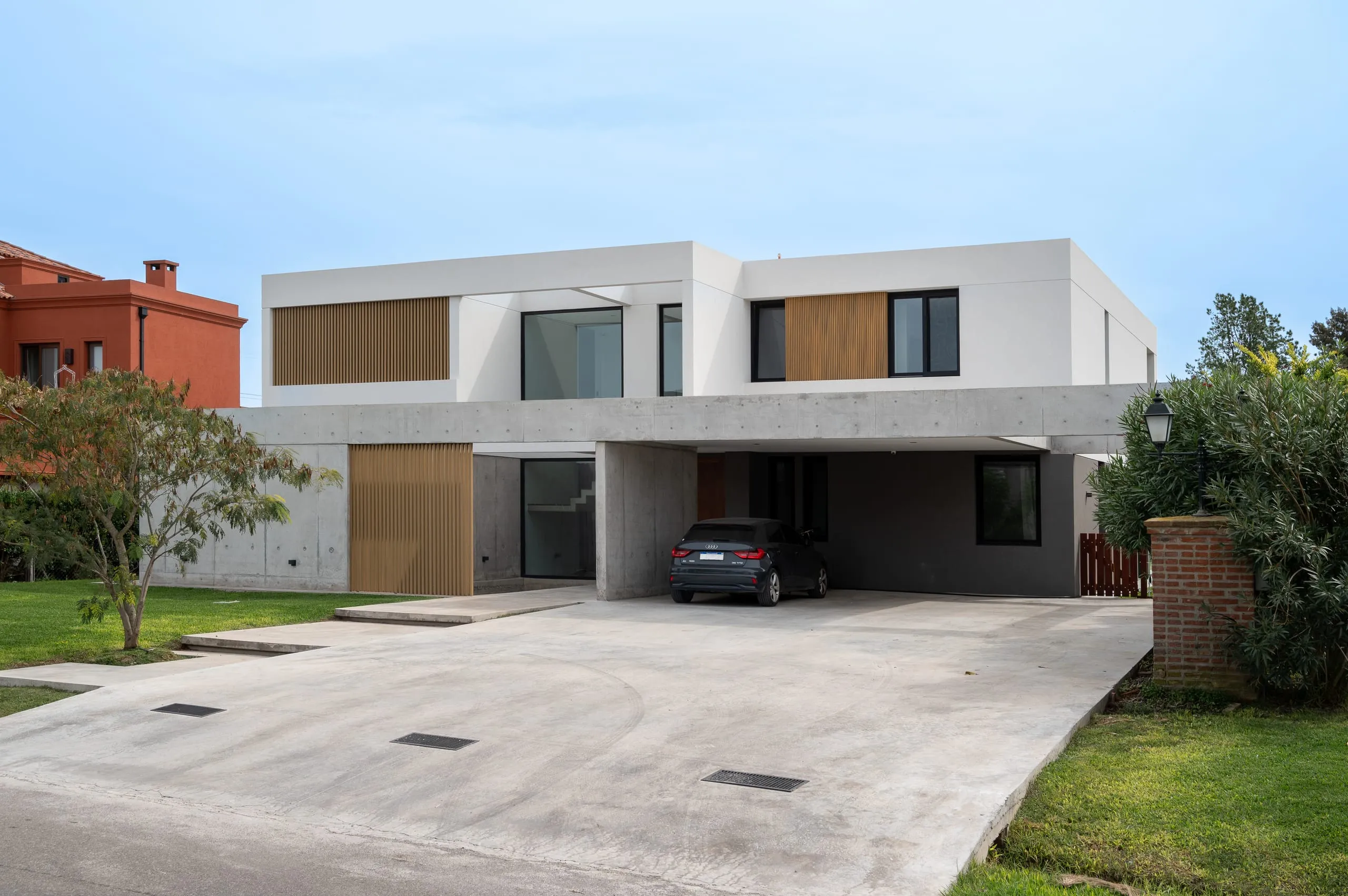 Fachada de acceso: volumen blanco sobre planta baja de hormigón visto, con cochera y revestimiento de madera