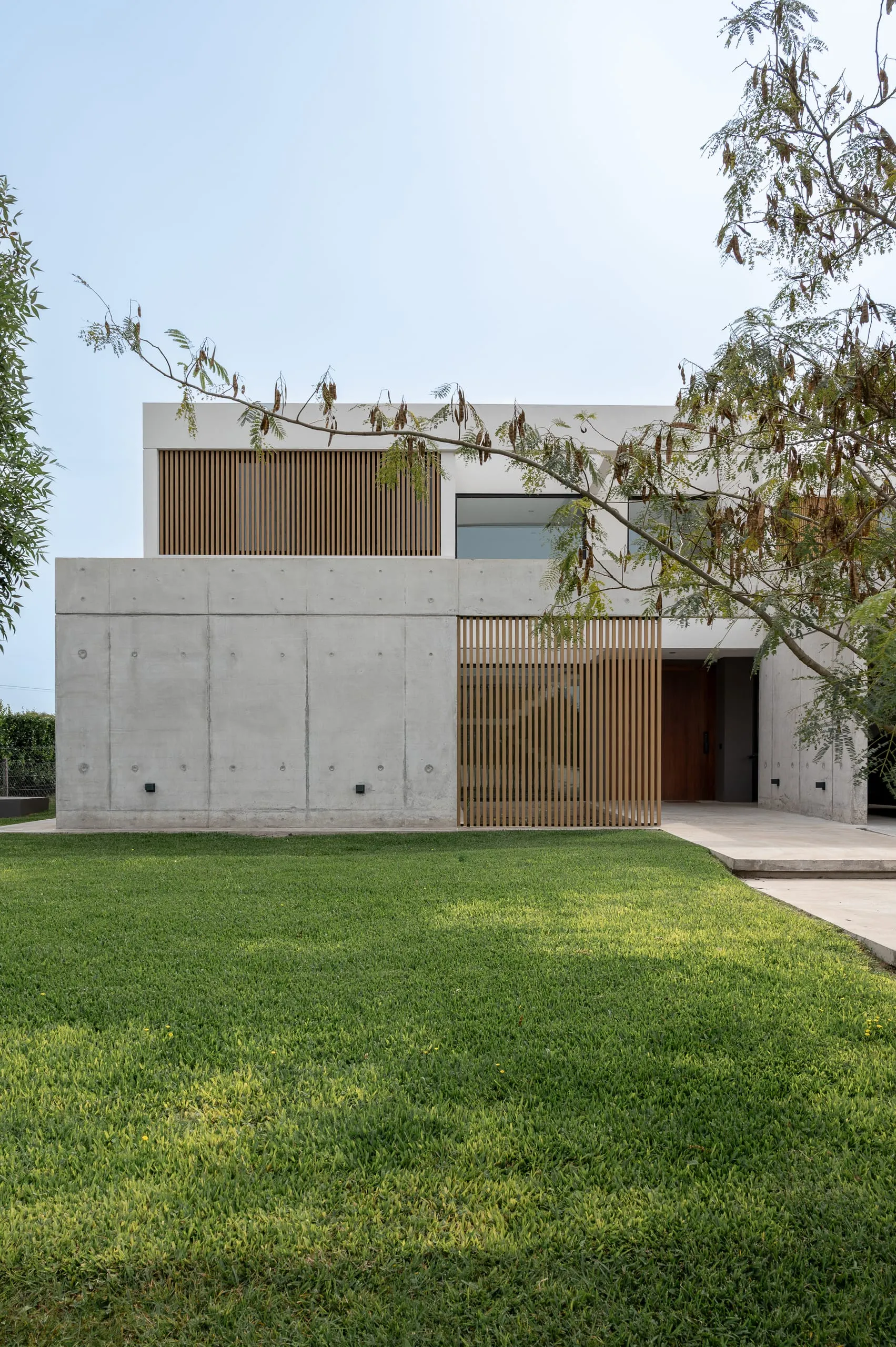 Frente de la casa desde el jardín, con portón de madera y muros de hormigón visto