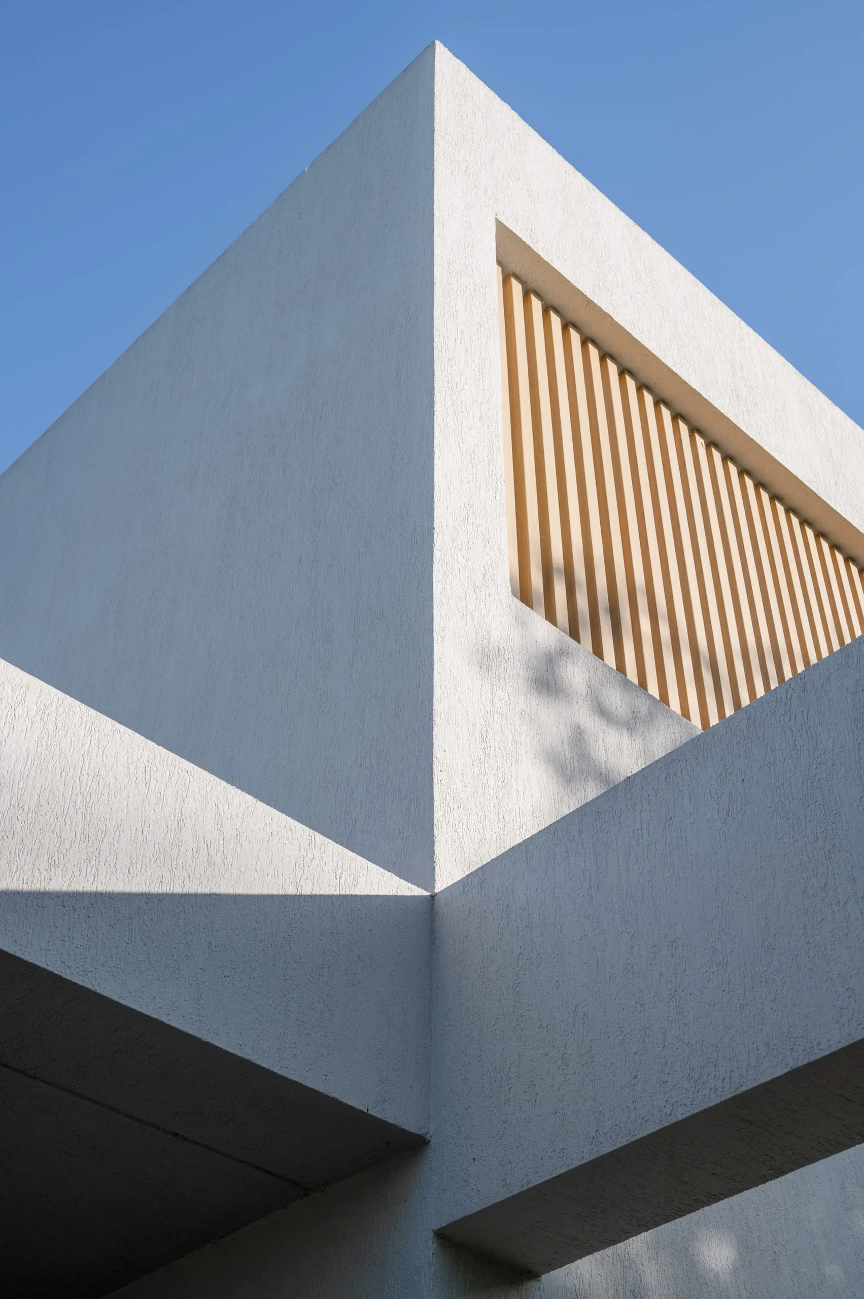 Detalle del volumen blanco con parasoles de madera contra el cielo
