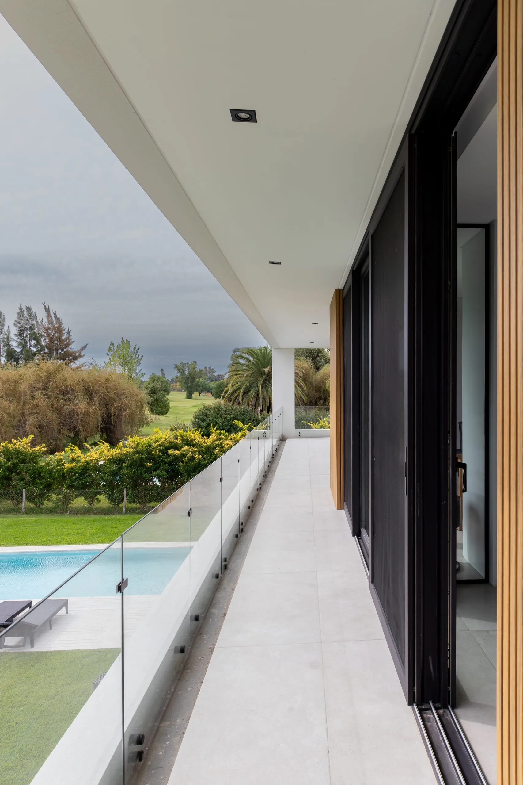 Galería de planta alta con baranda de vidrio y vista a la pileta y al jardín
