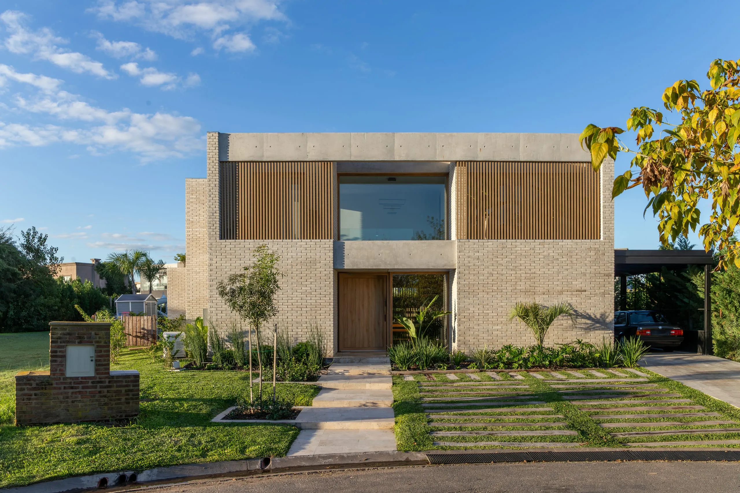 Frente con parasoles de madera, senda de acceso y jardín