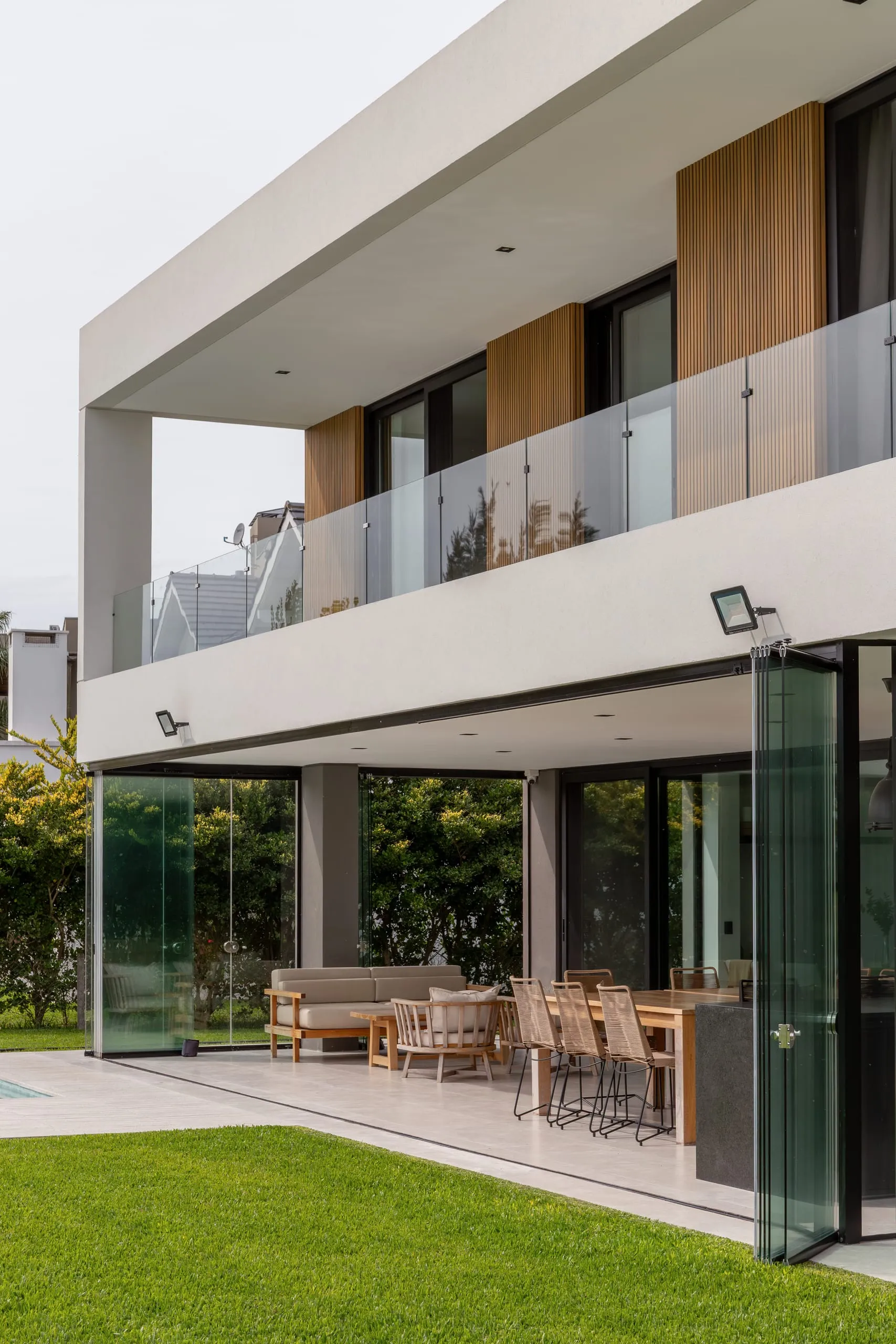 Galería de planta baja con carpinterías plegables abiertas y balcón de vidrio arriba