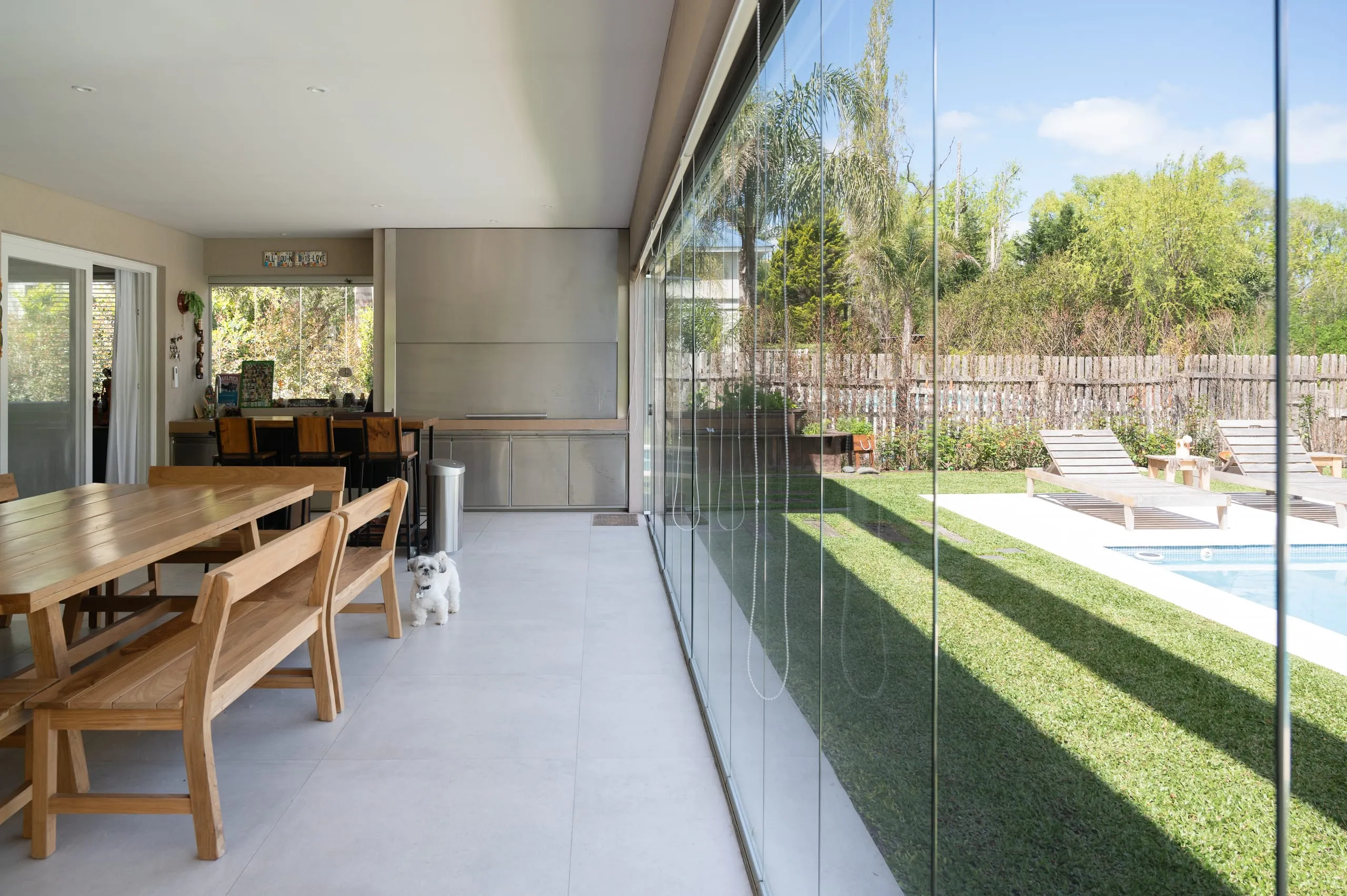 Comedor con mesa de madera junto al cerramiento vidriado hacia la pileta