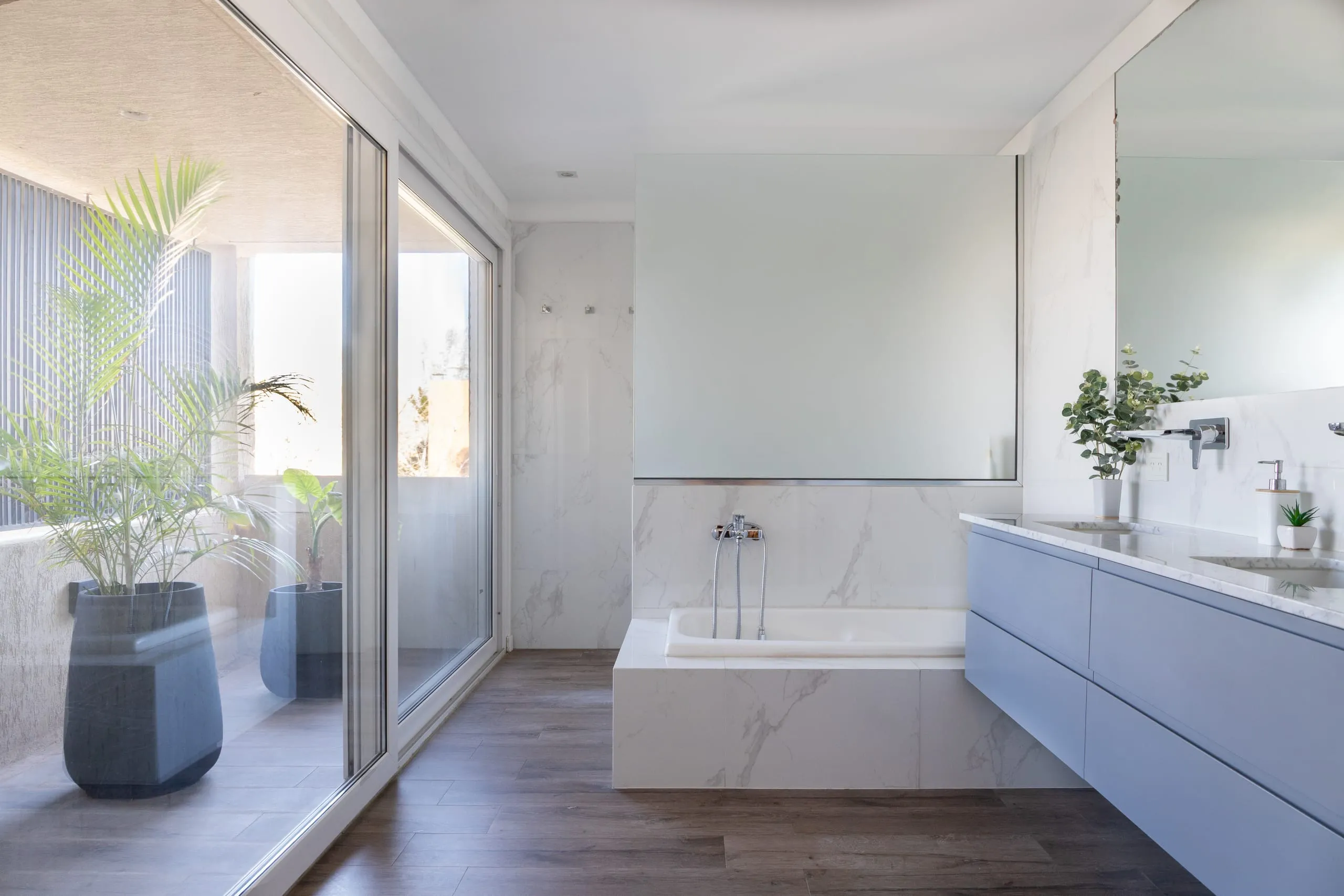 Baño principal con bañera, vanitory gris y ventanal con plantas