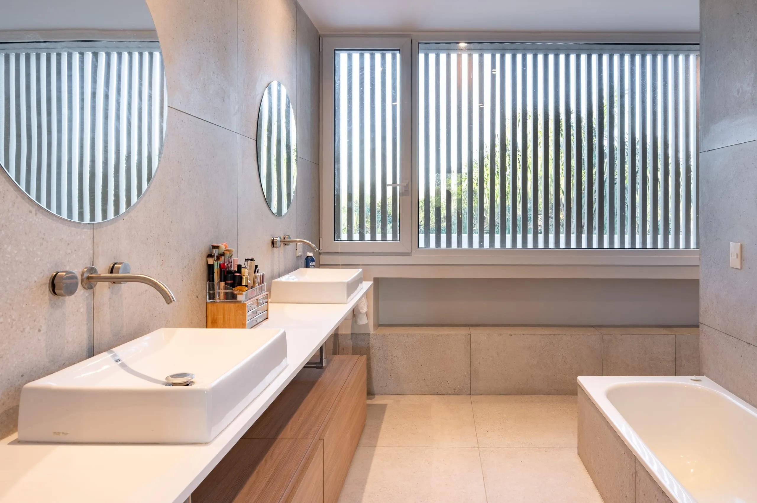 Baño principal con doble bacha, espejos redondos y bañera bajo la ventana