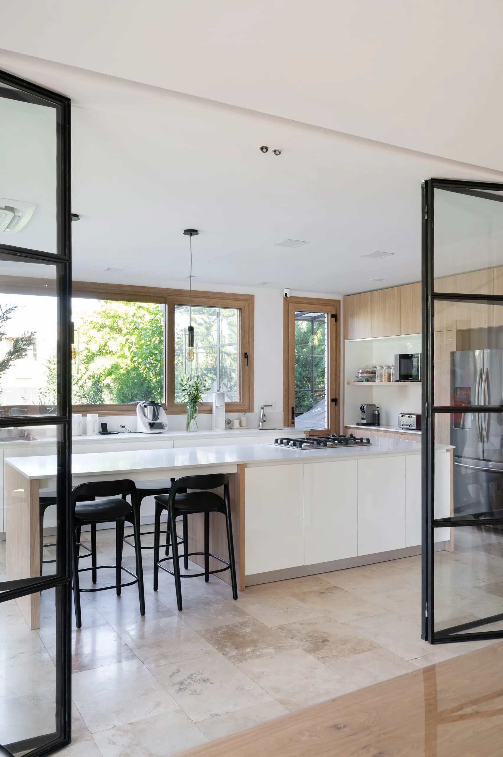 Cocina con isla blanca detrás de puertas de hierro y vidrio
