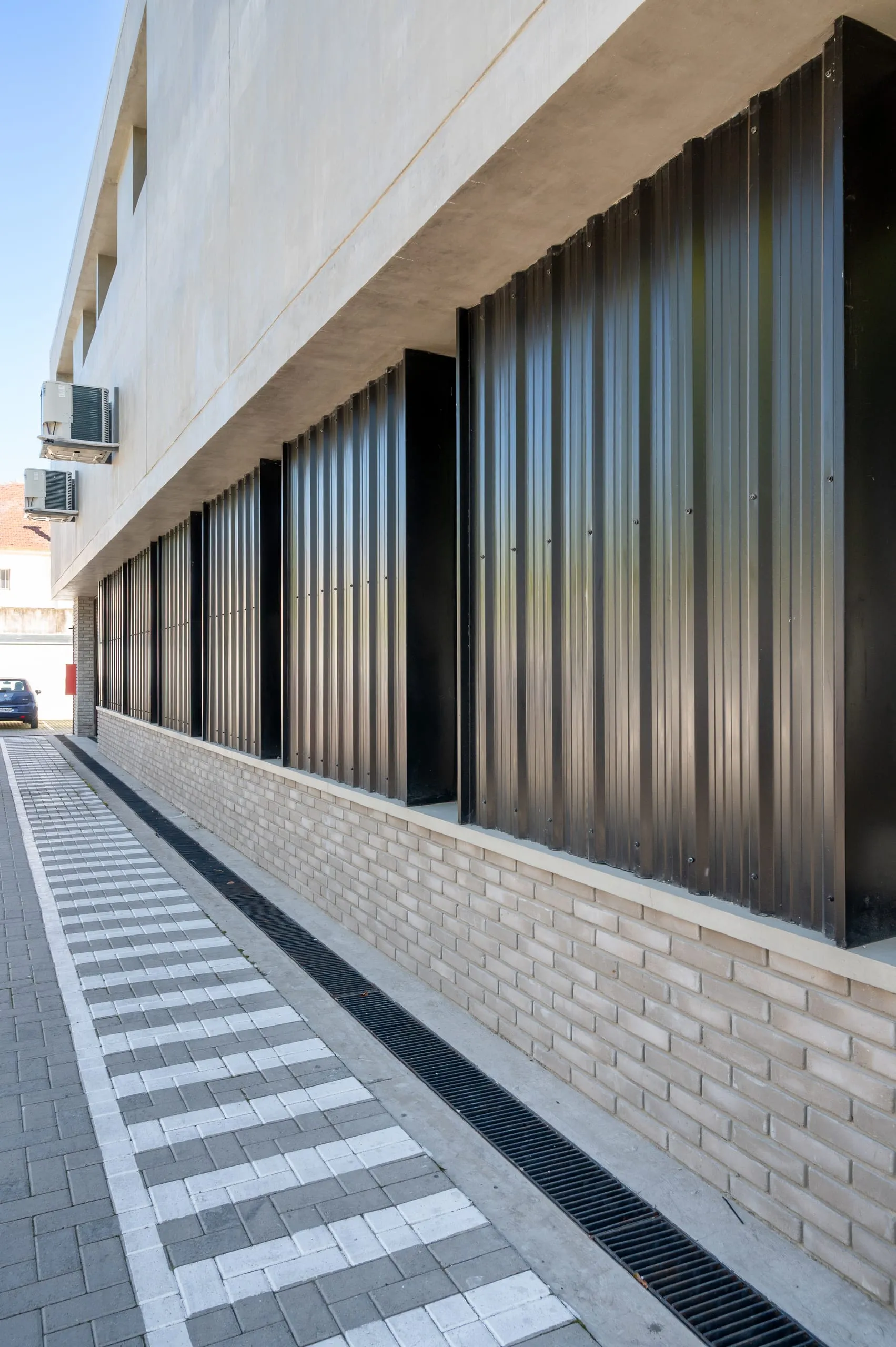 Fachada lateral con revestimiento negro y senda peatonal